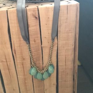 Necklace, gray ribbon, gold chain, green teardrop.